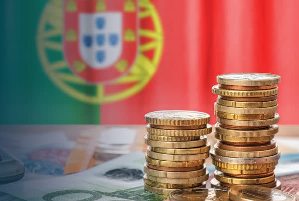 Coins and banknotes on a table with the Portuguese flag in the background